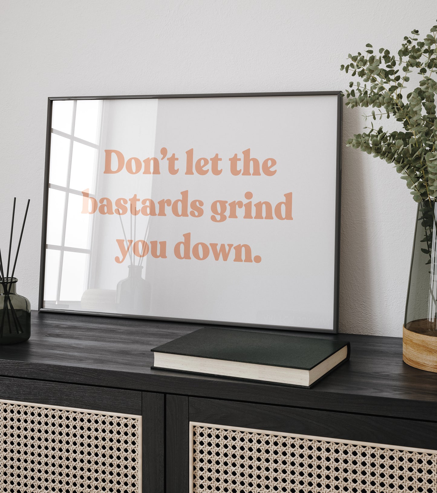 Framed 'Don't Let the Bastards Grind You Down' wall art sitting on in a modern living room side table.